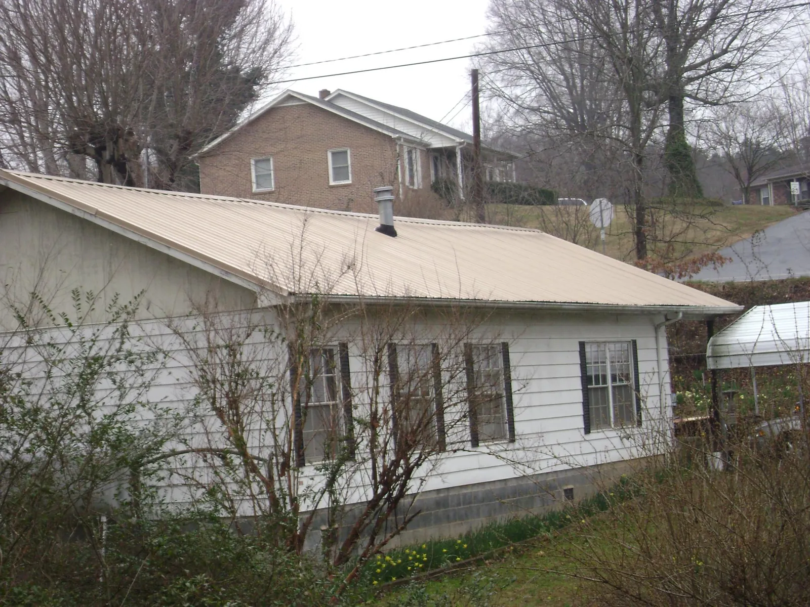 Tan metal roof on a white sided house set into a hillside — Commercial Roofing by Roofing Brothers in West Richland